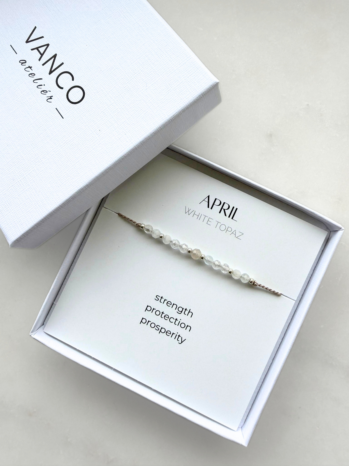White gift box with a white topaz bracelet. The bracelet is put on a card titled "April - White topaz".