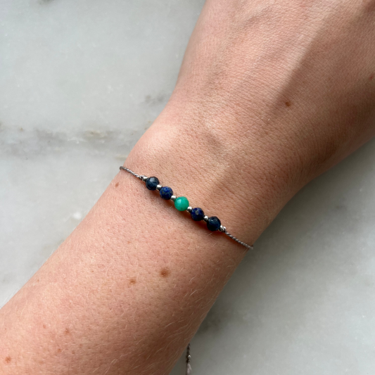 A female hand modeling a grey silk cord bracelet strung with these mineral beads: sapphire, amazonite, lapis lazuli, another amazonite and another sapphire. Between the minerals, there are also little gold beads separating them and making the design more elegant.