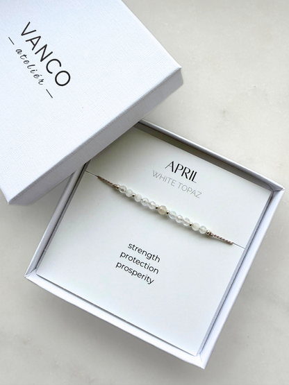 White gift box with a white topaz bracelet. The bracelet is put on a card titled "April - White topaz". 