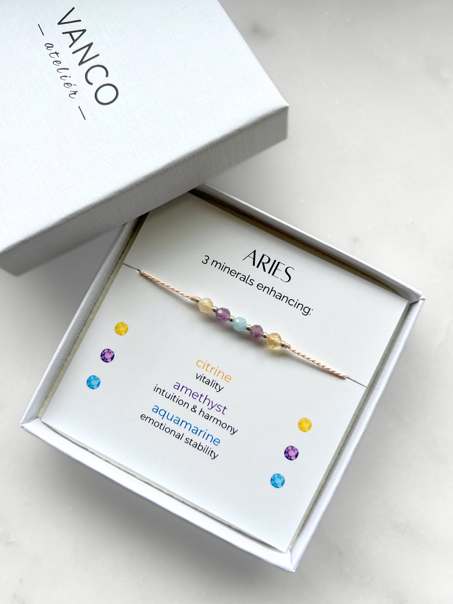 White gift box that contains a mineral bracelet for an Aries Zodiac sign. The bracelet is displayed on a card that describes the minerals and their meanings. There are five minerals on the bracelet: two citrines, two amethysts and aquamarine