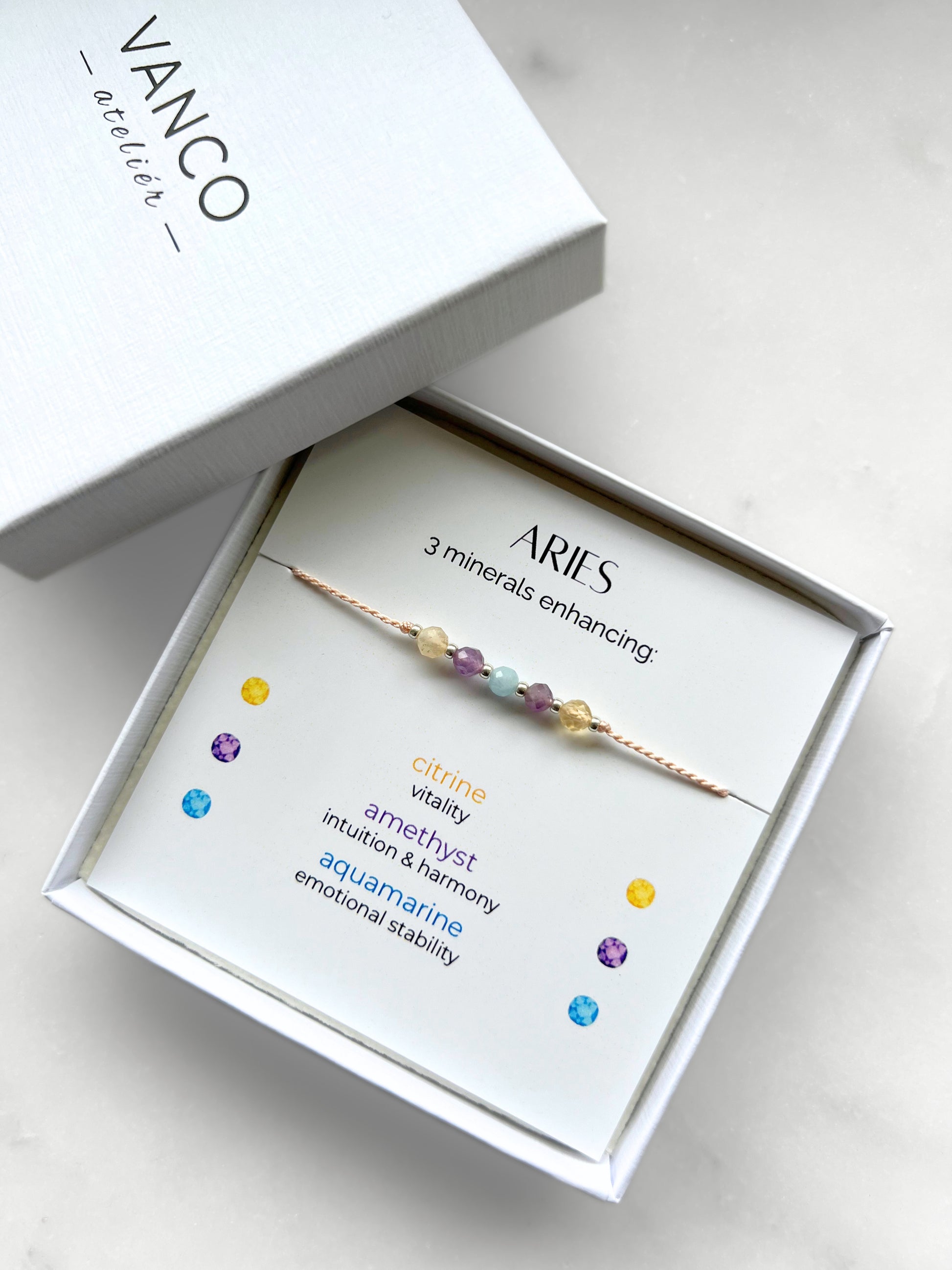 White gift box that contains a mineral bracelet for an Aries Zodiac sign. The bracelet is displayed on a card that describes the minerals and their meanings. There are five minerals on the bracelet: two citrines, two amethysts and aquamarine