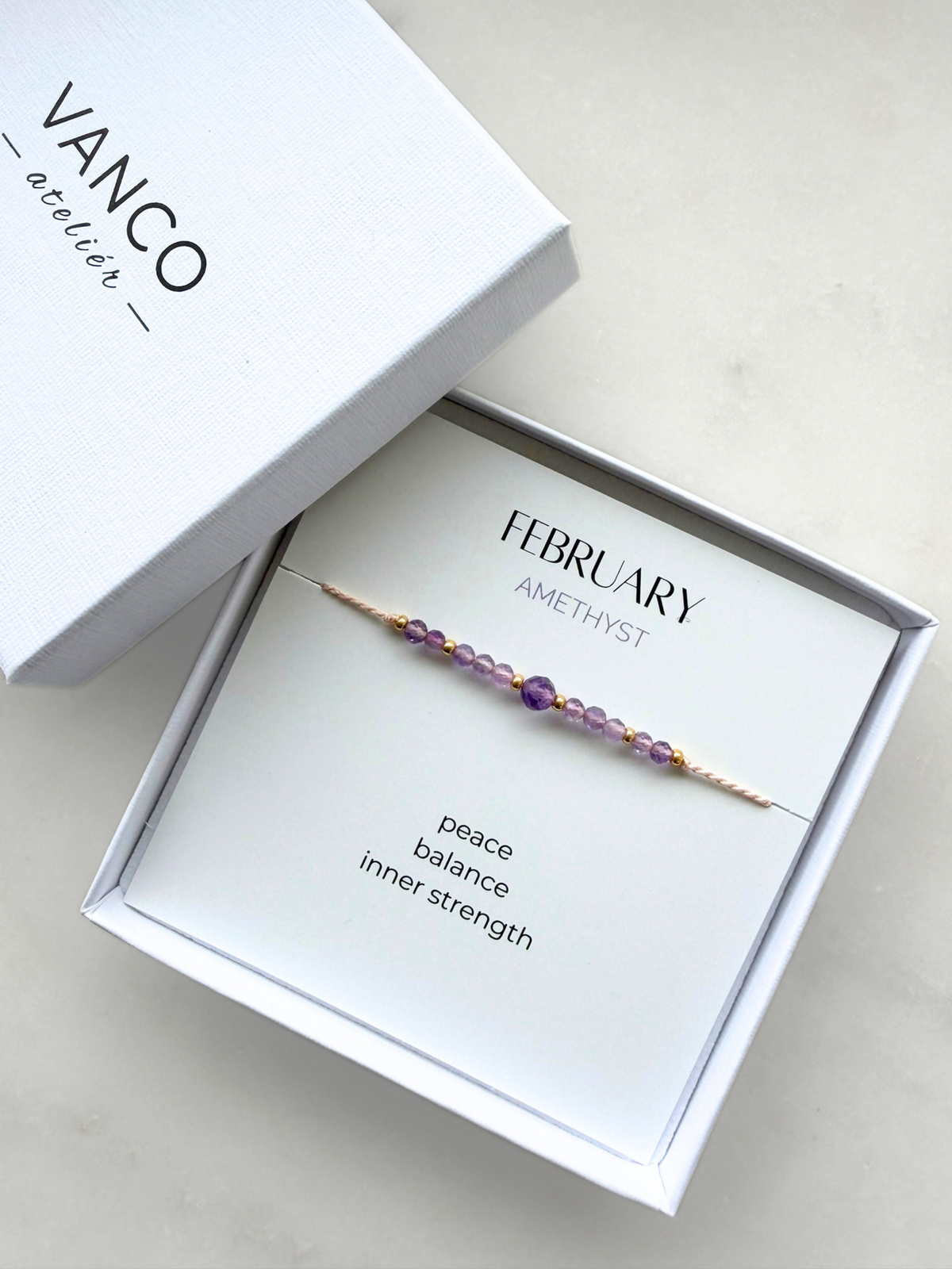 White gift box with an amethyst bracelet. The bracelet is put on a card titled "February Amethyst". 