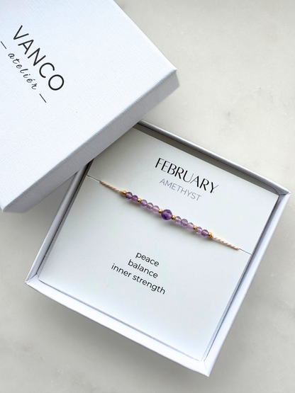 White gift box with an amethyst bracelet. The bracelet is put on a card titled "February Amethyst". 