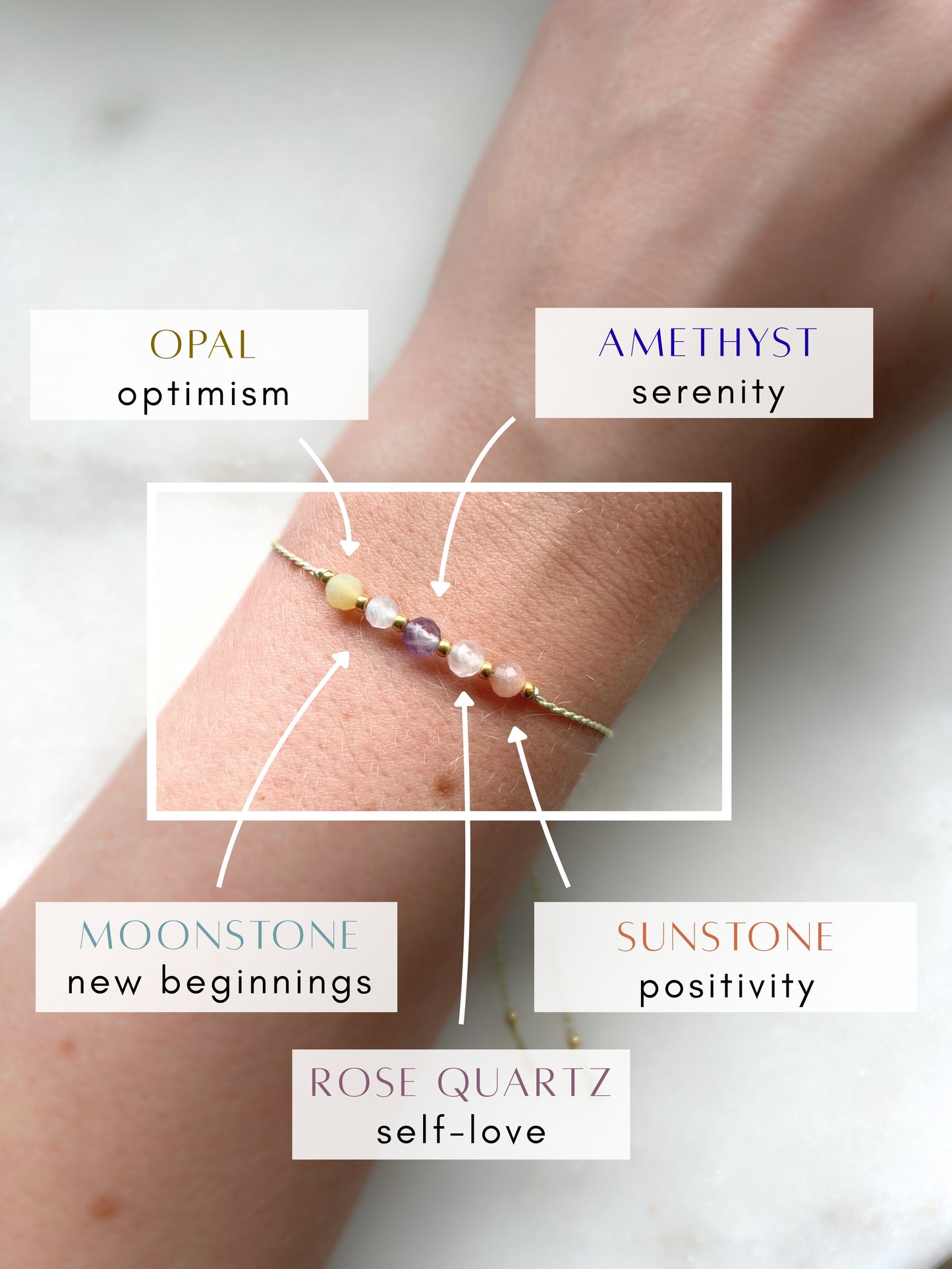 A female hand modeling a green silk cord bracelet strung with five mineral beads: purple amethyst, white moonstone, yellow opal, orange sunstone, rose quartz. Each mineral is separated from another with a little gold bead, making the design more elegant. Model is also wearing a dainty gold bracelet together with the mineral bracelet, showing how the two can be elegantly layered together.