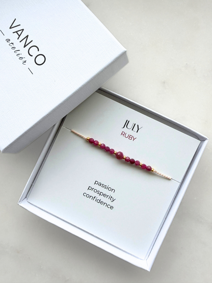 White gift box with a ruby bracelet. The bracelet is put on a card titled "July Ruby". 