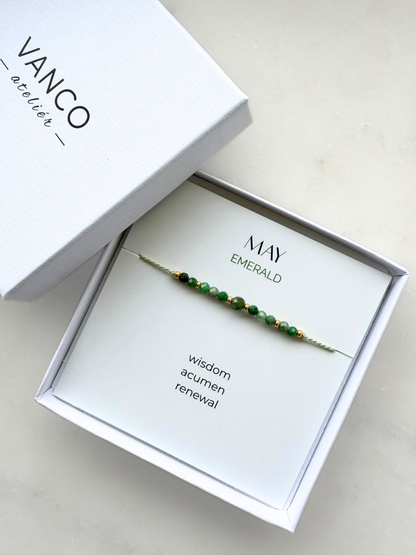 White gift box with an emerald bracelet. The bracelet is put on a card titled "May Emerald". 