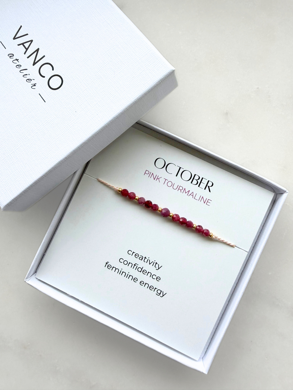White gift box with a pink tourmaline bracelet. The bracelet is put on a card titled "October - Pink tourmaline". 