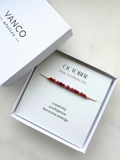 White gift box with a pink tourmaline bracelet. The bracelet is put on a card titled "October - Pink tourmaline". 