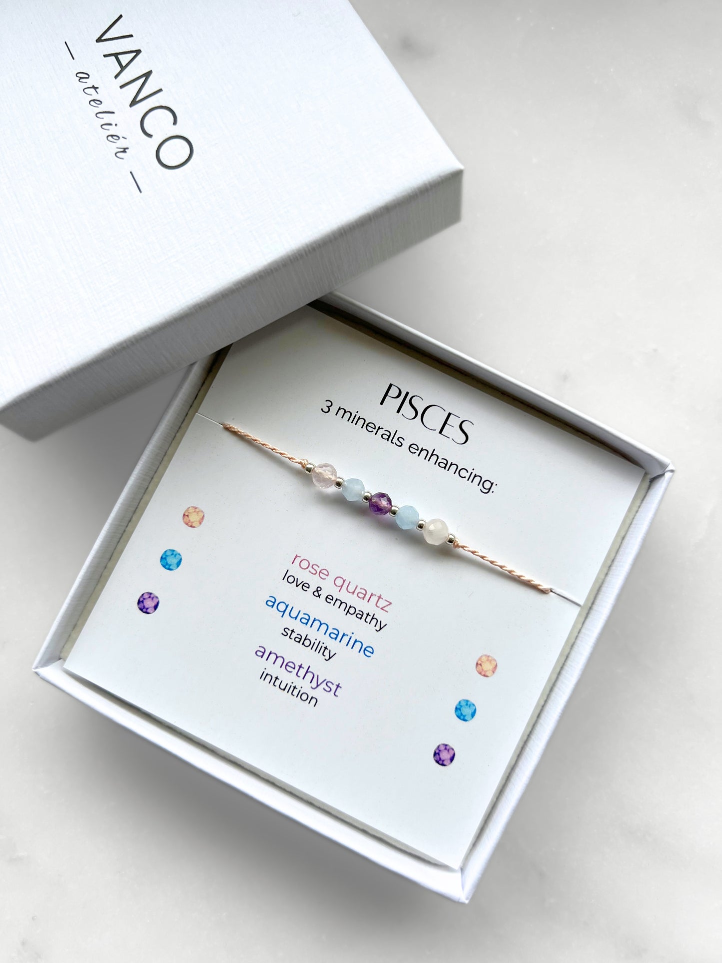 White gift box that contains a mineral bracelet for a Pisces Zodiac sign. The bracelet is displayed on a card that describes the minerals and their meanings. There are five minerals on the bracelet: two rose quartz, two aquamarines and amethyst