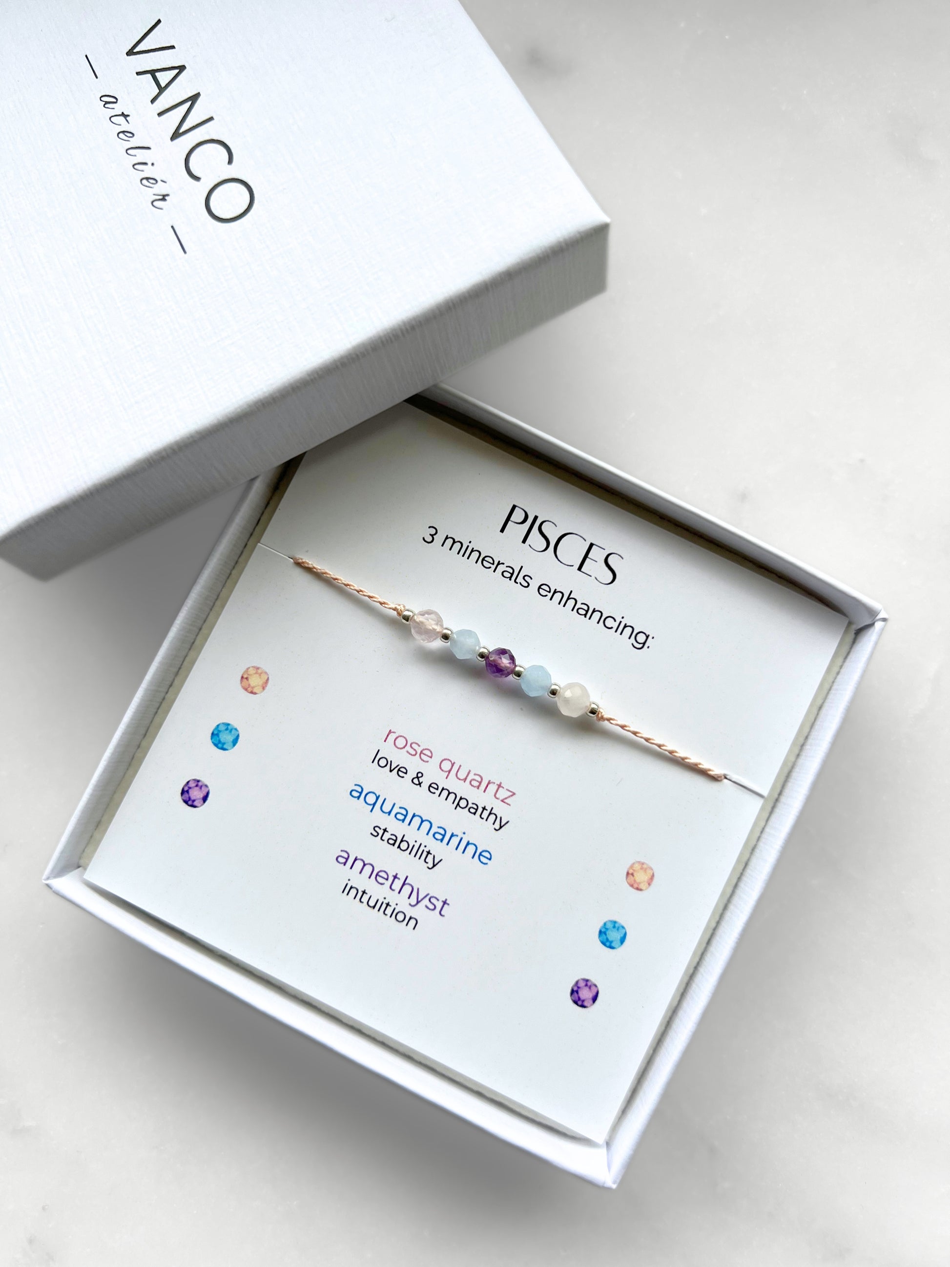 White gift box that contains a mineral bracelet for a Pisces Zodiac sign. The bracelet is displayed on a card that describes the minerals and their meanings. There are five minerals on the bracelet: two rose quartz, two aquamarines and amethyst