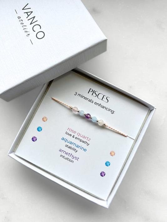 White gift box that contains a mineral bracelet for a Pisces Zodiac sign. The bracelet is displayed on a card that describes the minerals and their meanings. There are five minerals on the bracelet: two rose quartz, two aquamarines and amethyst