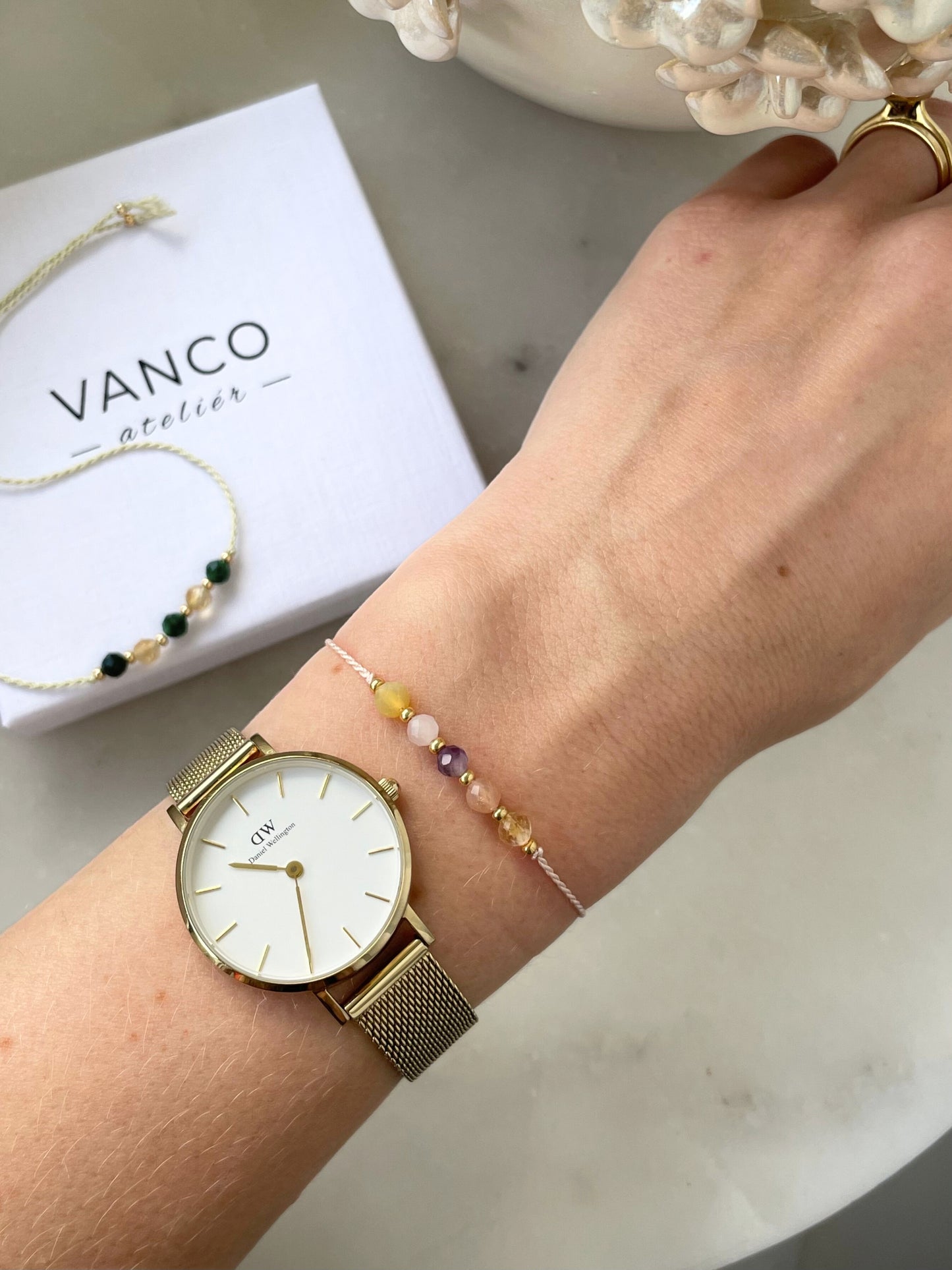 A female hand modeling a pink silk cord bracelet strung with five mineral beads: yellow citrine, orange sunstone, purple amethyst, rose quartz, yellow opal. Each mineral is separated from another with a little gold bead, making the design more elegant.