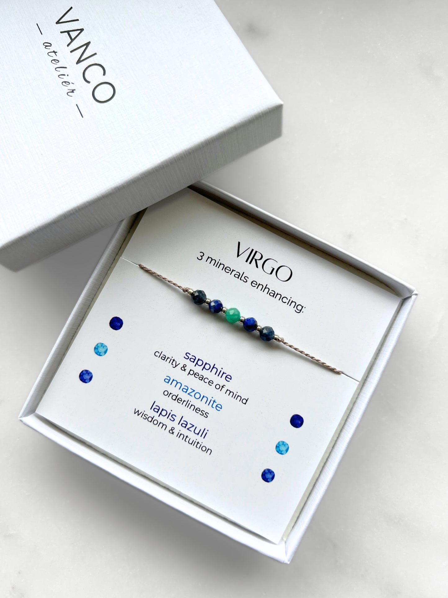White gift box that contains a mineral bracelet for a Virgo Zodiac sign. The bracelet is displayed on a card that describes the minerals and their meanings. There are five minerals on the bracelet: two sapphires, two amazonites and one lapis lazuli