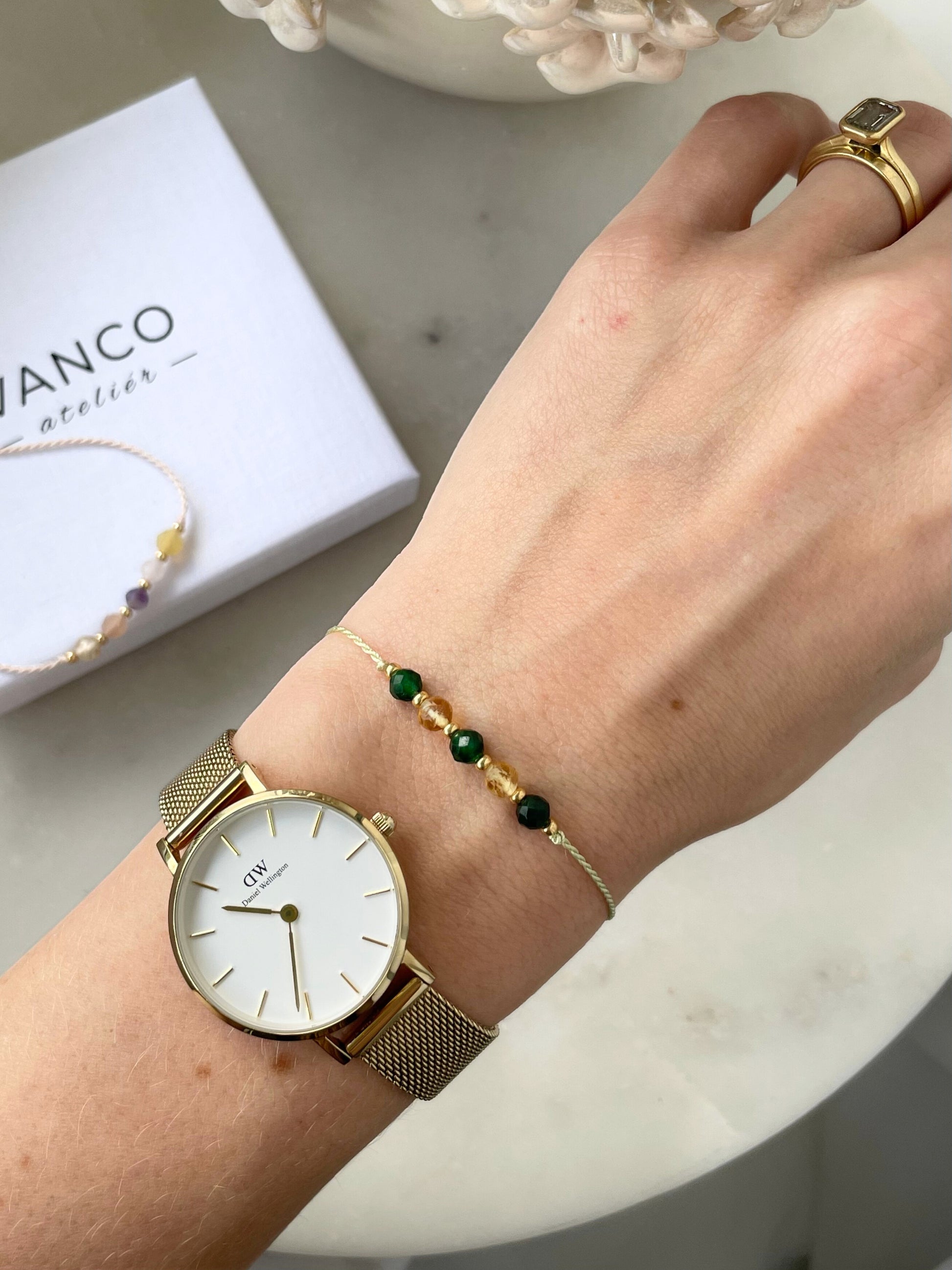 A female hand modeling a green silk cord bracelet strung with five mineral beads: alternating three green jades, two yellow citrines. Each mineral is separated from another with a little gold bead, making the design more elegant. Model is also wearing a dainty gold bracelet together with the mineral bracelet, showing how the two can be elegantly layered together.