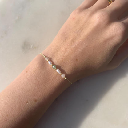 A female hand modeling a green silk cord bracelet strung with these mineral beads: white moonstone, white pearl, green aventurine, another pearl and rose quartz. Between the minerals, there are also little gold beads separating them and making the design more elegant.