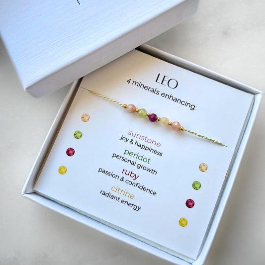 White gift box that contains a mineral bracelet for a Leo Zodiac sign. The bracelet is displayed on a card that describes the minerals and their meanings. There are five minerals on the bracelet: two sunstones, peridot, ruby and citrine