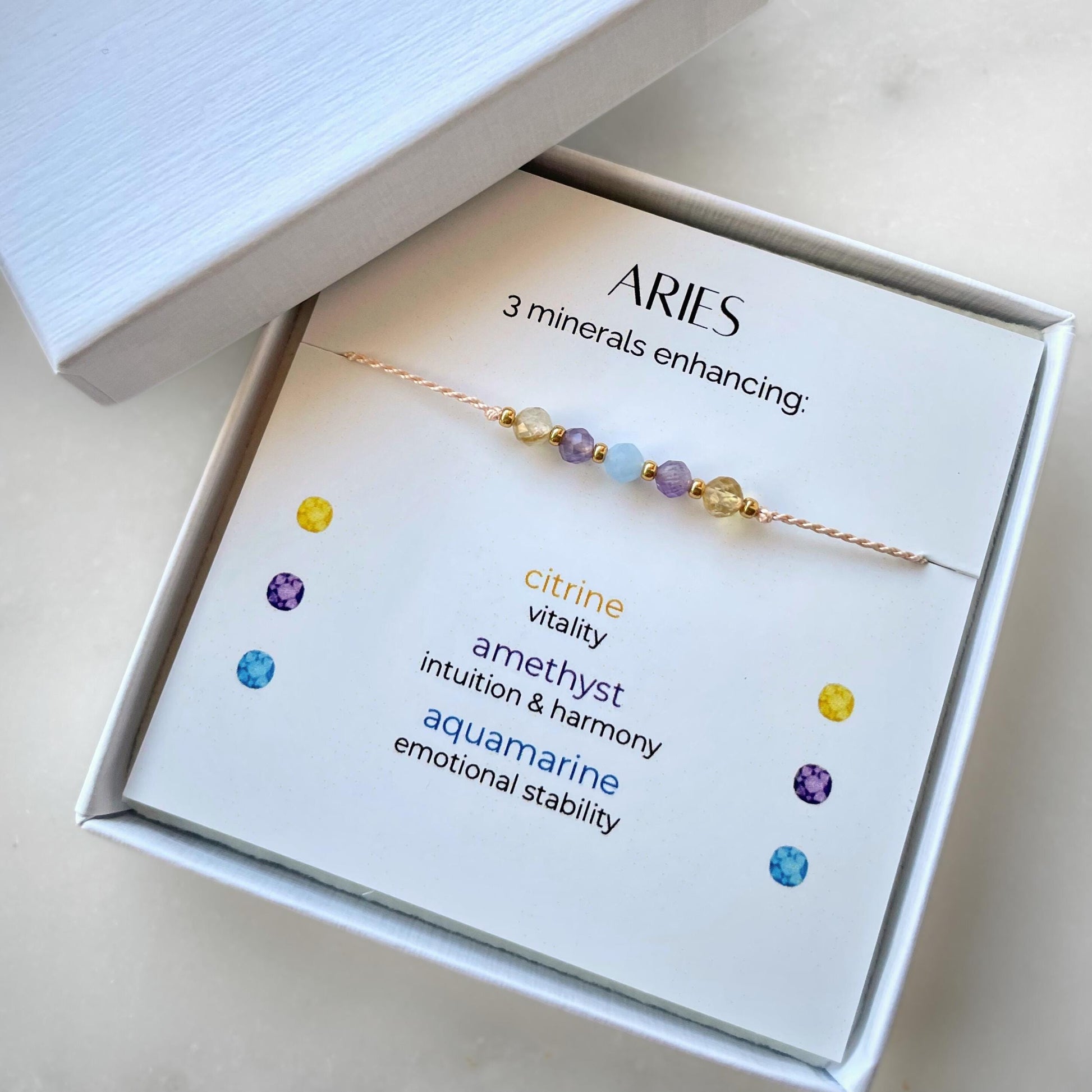 White gift box that contains a mineral bracelet for an Aries Zodiac sign. The bracelet is displayed on a card that describes the minerals and their meanings. There are five minerals on the bracelet: two citrines, two amethysts and aquamarine