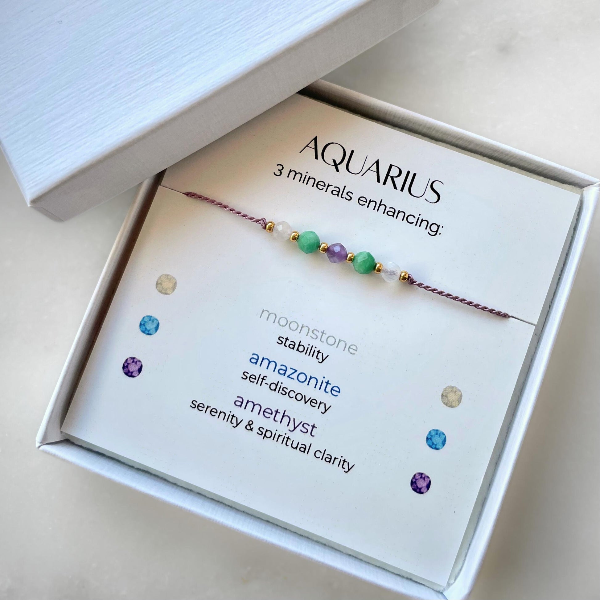 White gift box that contains a mineral bracelet for an Aquarius Zodiac sign. The bracelet is displayed on a card that describes the minerals and their meanings. There are five minerals on the bracelet: two moonstones, two amazonites and amethyst