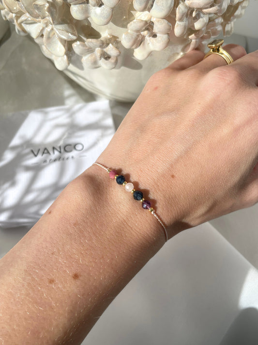 A female hand modeling a pink silk cord bracelet strung with five mineral beads: pink rhodonite, blue sapphire, rose quartz, blue sapphire, purple amethyst. Each mineral is separated from another with a little gold bead, making the design more elegant.