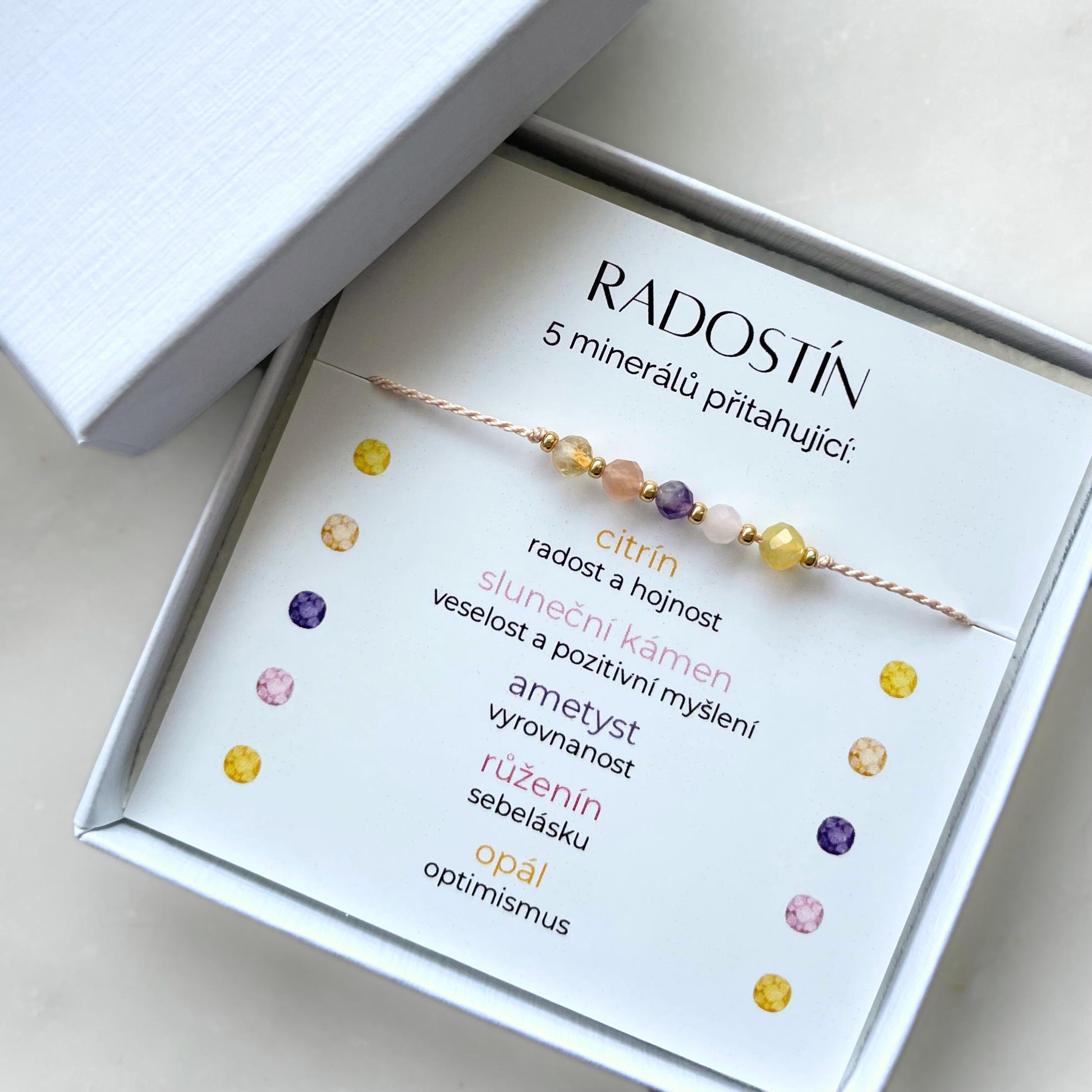 Náramek Radostín z 5 přírodních minerálů v dárkové krabičce. Karta v balení popisuje symboliku kamenů: Citrín pro radost a hojnost, sluneční kámen pro veselost a pozitivitu, ametyst pro vyrovnanost, růženín pro sebelásku, opál pro optimismus