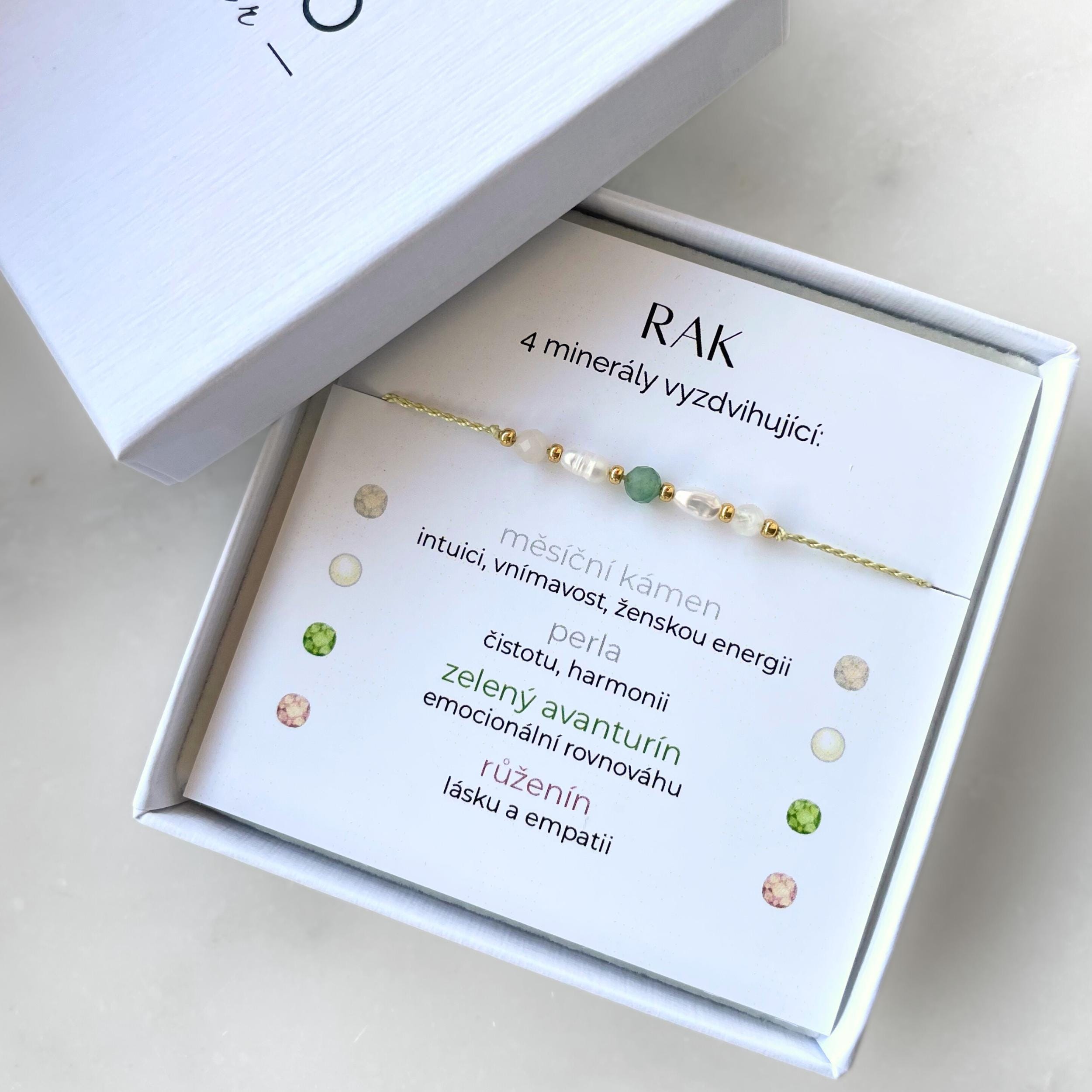 Jemný šňůrkový náramek pro znamení Rak v dárkové krabičce. Náramek je tvořený pěti drobnými broušenými minerály a zlatými korálky, a je uchycen na dárkové kartičce s nadpisem „RAK“. Na kartičce jsou vypsány použité kameny a jejich význam: Měsíční kámen pro intuici, vnímavost, ženskou energii; perla pro čistotu a harmonii; avanturín pro emocionální rovnováhu; růženín pro lásku a empatii