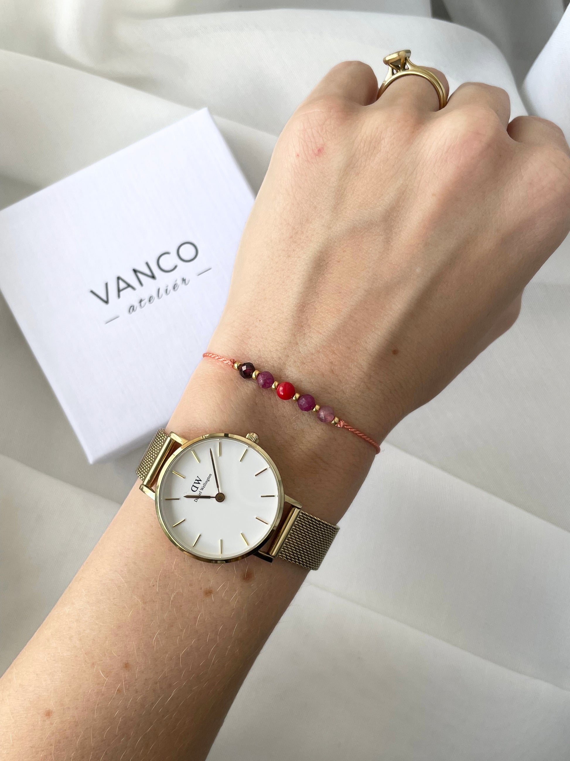 A female hand modeling a pink silk cord bracelet strung with five mineral beads: pink tourmaline, red ruby, red coral, another ruby and red garnet. Each mineral is separated from another with a little gold bead, making the design more elegant.