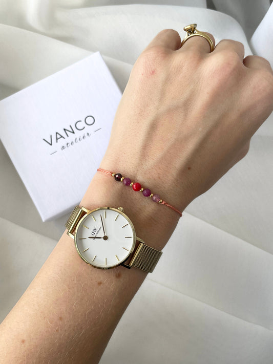 A female hand modeling a pink silk cord bracelet strung with five mineral beads: pink tourmaline, red ruby, red coral, another ruby and red garnet. Each mineral is separated from another with a little gold bead, making the design more elegant.